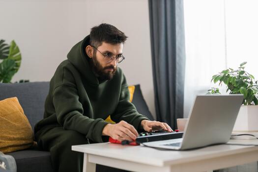 Man recording music track with portable midi keyboard on laptop computer in home studio. Producing and mixing music beat making and arranging audio content with professional audio devices close-up photo