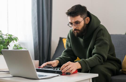 portrait Man recording electronic music track with portable midi keyboard on laptop computer in home studio. Producing and mixing music beat making and arranging audio content photo