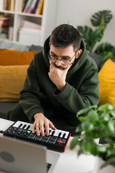 Close-up Man recording electronic music track with portable midi keyboard on laptop computer in home studio. Producing and mixing music beat making and arranging audio with professional audio devices photo