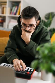 Close-up male music producer or arranger using laptop and midi keyboard and other audio equipment to create music at home studio. Beat making and arranging audio content and composing song concept photo