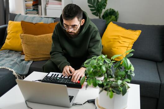 Close-up Guy music producer or arranger using laptop and midi keyboard and other audio equipment to create music at home studio. Beat making and arranging audio content and composing song concept photo