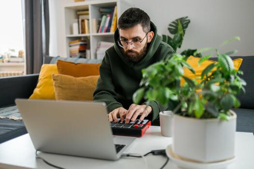 bearded Man recording electronic music track with portable midi keyboard on laptop computer in home studio. Producing and mixing music beat making and arranging audio content photo
