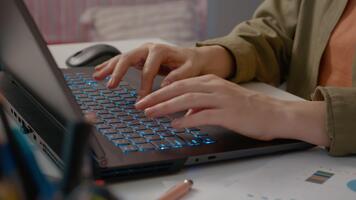 Frau Typen auf ein Laptop im ein Zuhause Büro. ihr Hände Bewegung schnell über das beleuchtet Klaviatur, präsentieren ein effizient Arbeitsplatz mit Unterlagen und Schreibwaren. video
