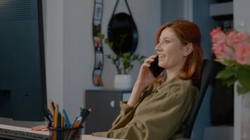 glad kvinna multitasks i henne Hem kontor, skriver på henne dator medan njuter en telefon konversation. henne arbetsyta är organiserad och inbjudande. video