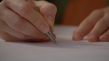 två händer tecken en kontrakt på en skrivbord täckt med ark av papper, visa upp de fokus och tillägnande av avlägsen arbete i en mysigt kontor miljö. video