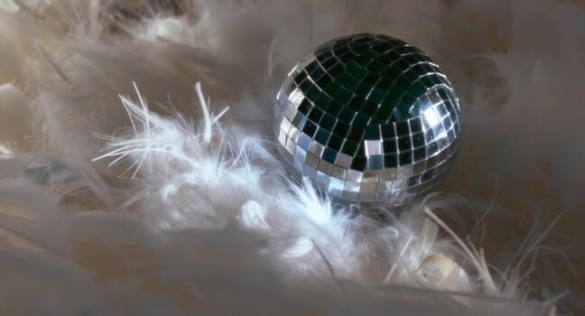 Sparkling disco ball nestled amongst fluffy feathers reflects light, creating a whimsical and festive atmosphere for parties and special events photo