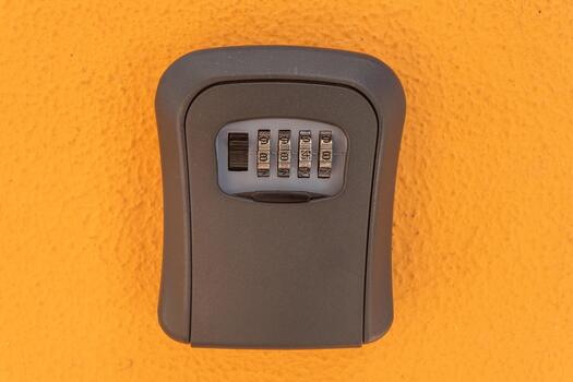 A gray lockbox with a combination dial is attached to a vibrant orange wall, providing a secure place to store keys for easy access photo