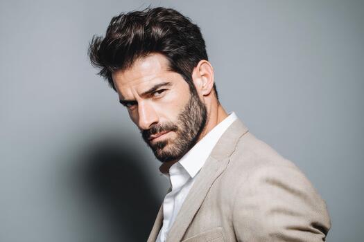 Bearded man wearing a suit looking intensely at the camera against a plain gray background photo