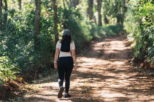 Young woman walking alone on a dirt path in a serene forest surrounded by lush greenery and sunlight filtering through trees on a peaceful day photo