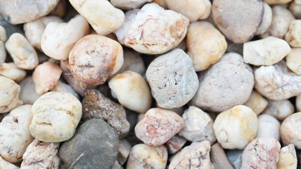 A Close Up View of a Variety of Smooth River Stones in Natural Earth Tones Surrounded by Sand and Tiny Rocks Creating a Textured Background photo