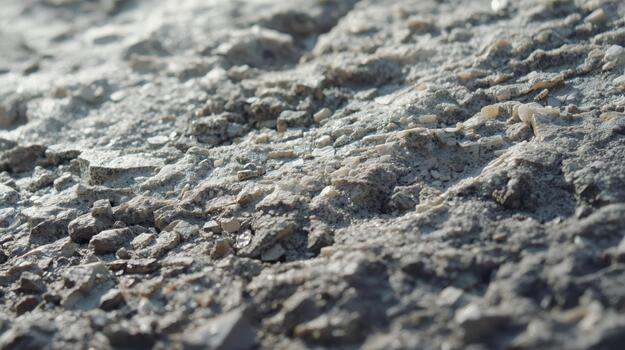 A textured gray concrete surface with tiny embedded rocks is shown in a close-up shot under bright light, presenting a rough, gritty texture. photo