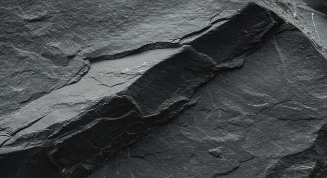 Close up of dark gray slate rock surface shows natural layers and texture in stone quarry with rough and jagged edges formed by geology. photo