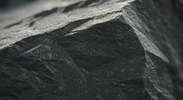 Close up of a dark grey stone surface showing its rough texture and edges illuminated by soft natural light to enhance details. photo