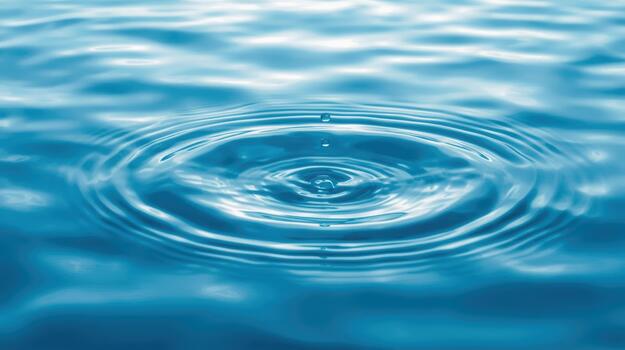 Water drop creates concentric circles of ripples in a tranquil blue expanse of liquid surface with a mesmerizing hypnotic pattern forming above. photo