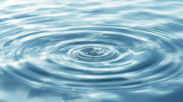 A single droplet creates delicate circular ripples on the calming surface of the clear blue water showing beautiful concentric waves spread out. photo