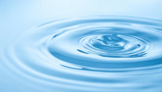 A mesmerizing close up captures the gentle concentric ripples spreading across the calm surface of crystal clear blue water after a drop. photo