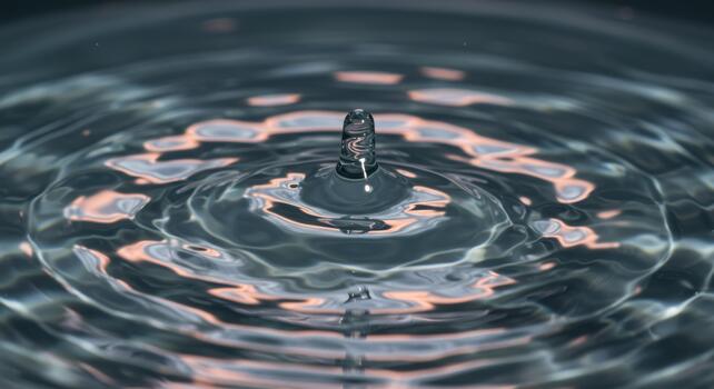 A single water droplet creates ripples and concentric circles across the surface of a body of water, showcasing liquid dynamics and texture. photo