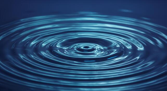 A single drop of water creates concentric circular ripples on the deep blue surface of a calm liquid forming a beautiful pattern. photo