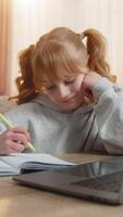 Young girl feeling tired and lazy while doing homework at table with laptop at home. Caucasian child writing in notebook, expressing boredom and exhaustion during her study time, reflecting struggle video