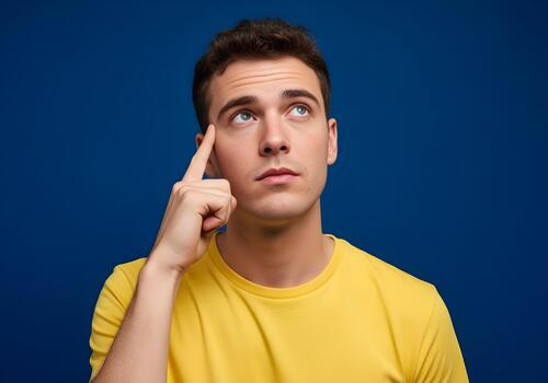 Young man deep in thought contemplating options and ideas for future projects looking up against a solid blue background symbolizing imagination and creative problem solving photo