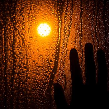 Abstract rainy window view with hand silhouette and blurred golden light evoking reflection and introspection creating mood of quiet contemplation photo