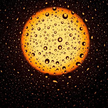 Abstract view of raindrops on glass with a diffused golden light source casting a warm glow and creating a unique atmospheric effect photo