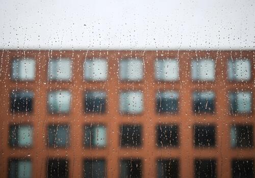 Rainy Day View Through Window with Water Droplets and Blurred Building Facade Creating a Sense of Isolation and Urban Atmosphere photo