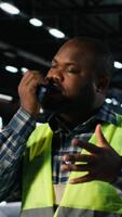 vertikal svart ingenjör samtal in i walkie prat och övervakning tillverkning verktyg i en verkstad, demonstrera stark arbetskraft medverkan och utveckling för aktivitet inom industri växt. kamera b. video