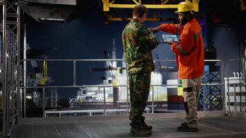 Security officer in camouflage uniform monitors offshore drilling operation, using radio communication for intelligence coordination and threat detection in maritime environments. Camera A. video