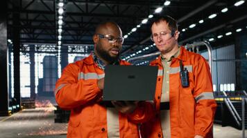 diverso operatori uso il computer portatile per coordinata produzione attività su il fabbrica pavimento, evidenziazione manodopera e il industriale ambiente per pesante produzione e logistica compiti. telecamera b. video