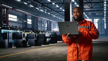 tekniker förvaltar drift förfaranden med handhållen bärbar dator, highlighting teknik ansvar och arbetskraft styrka medan han promenader runt om på de fabrik golv. verkstad tillverkning. kamera a. video