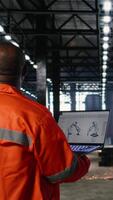 vertikal arbetstagare använder sig av automatisering programvara ansluten till robot maskineri via bärbar dator, omgiven förbi metall Utrustning och tillverkning verktyg. industriell miljö slingor teknik. kamera a. video
