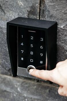 Modern digital keypad with a sleek design, featuring a user pressing the button, set against a textured stone wall, illustrating advanced security technology and convenience photo