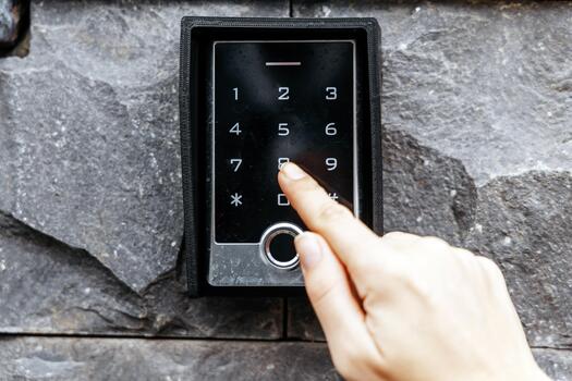 Hand of a person pressing a number on a modern digital keypad mounted on a textured stone wall, illustrating security access technology and user interaction photo