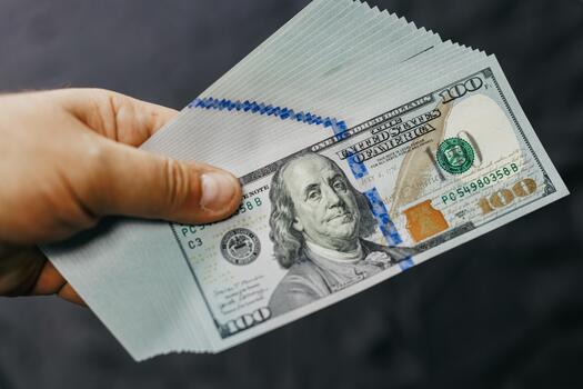Hand holding a stack of hundred-dollar bills, showcasing detailed currency design, with a focus on the intricate patterns and textures of the banknotes in a neutral background photo