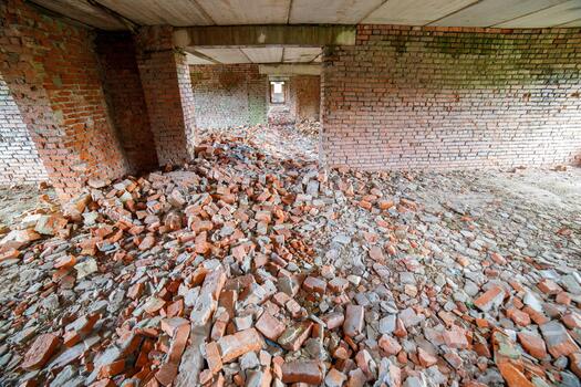 Large quantity of broken bricks and rubble scattered across the interior of an abandoned building. The scene conveys a somber and desolate mood, highlighting destruction and neglect. photo