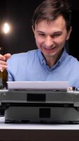 vertical Man smiling and enjoying the process of typing on an antique manual typewriter with a blank page, an empty bottle suggesting a creative, introspective writing session video