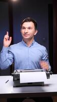 verticaal jong volwassen Mens zittend Bij een bureau, op zoek omhoog en richten een vinger, ervaren een plotseling idee terwijl gebruik makend van een oud mechanisch schrijfmachine met een blanco bladzijde video