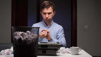 frustriert Mann knirschend ein Stück von Papier, Sitzung beim ein Schreibtisch überfüllt mit zerknittert Blätter, Nächster zu ein alt Schreibmaschine, bedeuten ein Kampf mit des Schriftstellers Block video