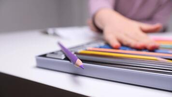 Child's hand reaching for a purple colored pencil, lying on a white table with an open set of pencils, emphasizing early learning, creativity, and artistic development video
