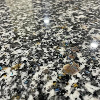 Close up view of a speckled granite countertop with a reflective surface showing subtle light glints and varied mineral patterns photo