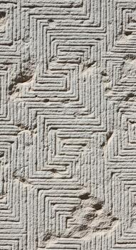 Intricate geometric pattern carved into textured stone surface with repeating labyrinthine design photo