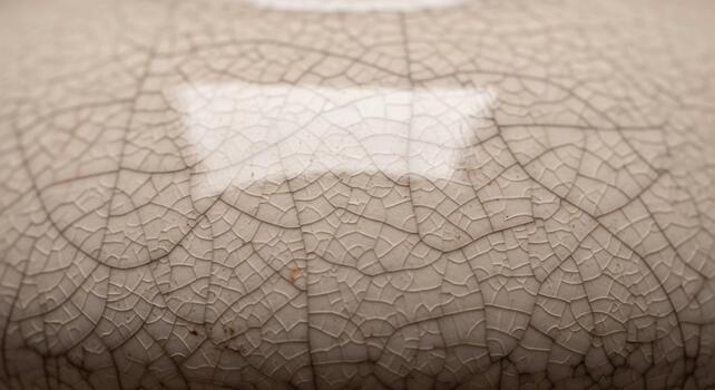 Close up of a textured ceramic surface with a network of fine cracks and a bright rectangular reflection photo
