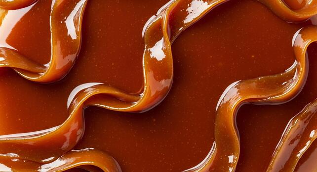 Close up macro shot of rich liquid caramel sauce dripping and swirling in abstract patterns creating a decadent sweet texture photo