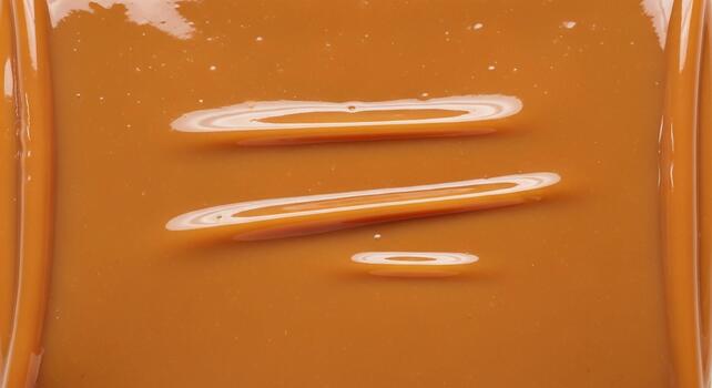 Close up abstract view of glossy caramel colored liquid with swirling patterns and reflections photo