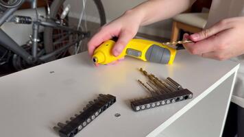 närbild av händer byta borra bit på en gul sladdlös kraft borra medan välja de rätt storlek på en vit tabell, inomhus. video