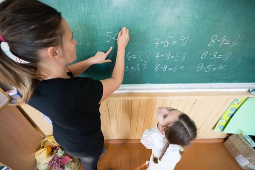 Teacher and student at chalkboard learning arithmetic equations. Classroom setting emphasizing learning and education. photo