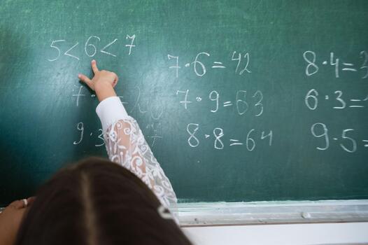 Child points to math problems on a green chalkboard, showcasing classroom learning and mathematical concepts being taught in the learning environment. photo