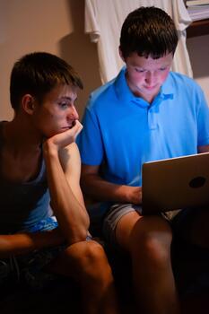Two young men engrossed in a laptop display. The first man looks on thoughtfully. The second man is focused intently on the screen. photo