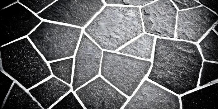 A black and white close up of irregular stone pavement with white grout lines creating a dynamic textured background photo